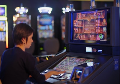 A person is seated at a slot machine console in a casino, focusing intently on the game displayed on the screen. The background shows several other illuminated gaming machines, adding a vibrant and colorful atmosphere to the scene.