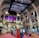 The interior of a large, ornately designed building with arched ceilings and intricate architectural details. The space features gaming machines lined up along the floor, under a high ceiling with a grid pattern. Lighting in purple and white tones enhances the ambiance.