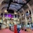 The interior of a large, ornately designed building with arched ceilings and intricate architectural details. The space features gaming machines lined up along the floor, under a high ceiling with a grid pattern. Lighting in purple and white tones enhances the ambiance.